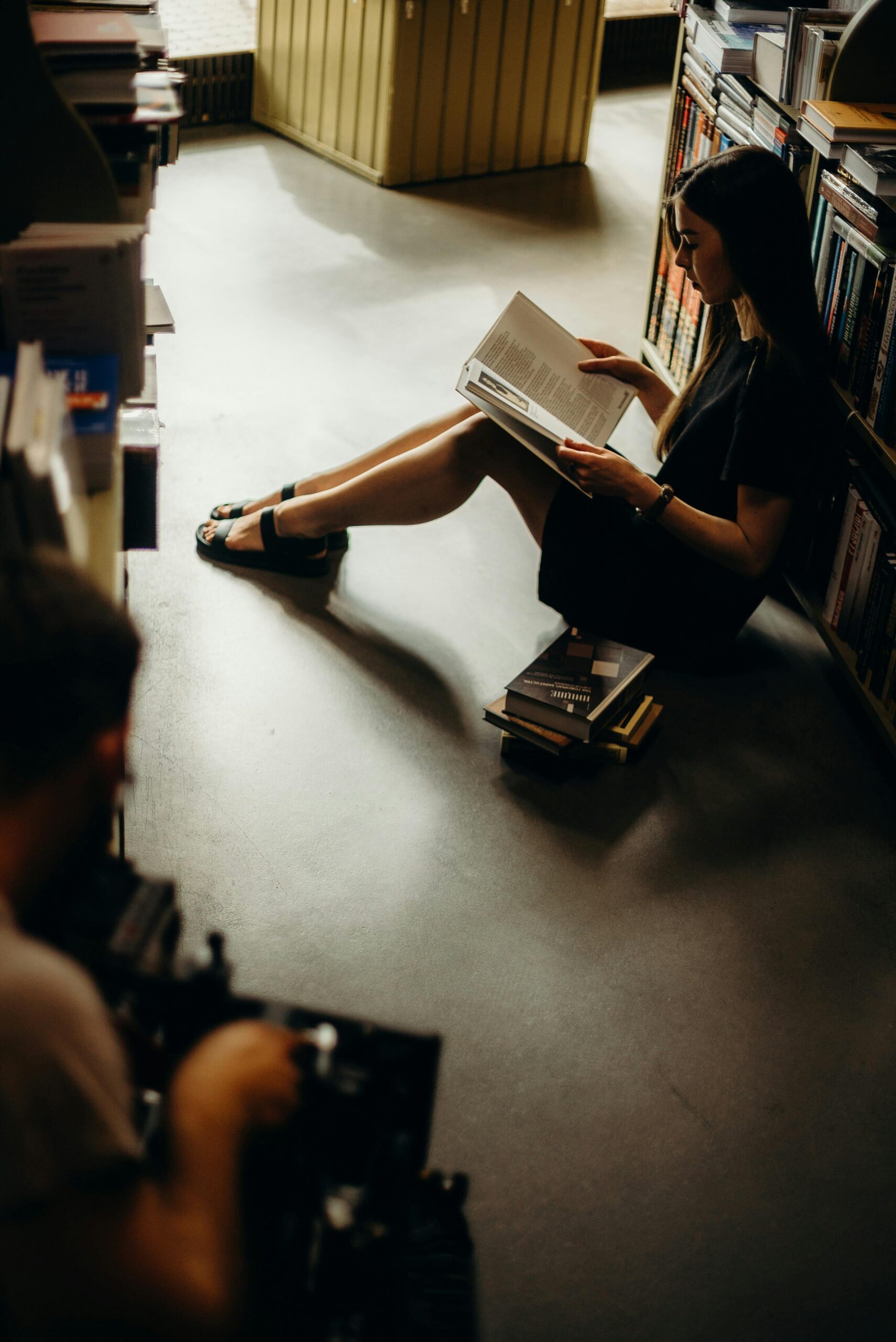 Атмосфера книжного магазина «Подписные издания» Посетительница читает книгу, сидя на полу среди книжных полок в «Подписных изданиях»